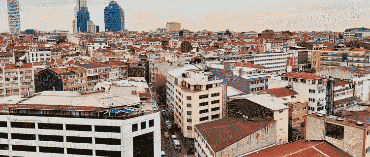 Istanbul from a rooftop under an overcast sky: a crowd of low apartment blocks and terracotta roofs, a street running down between them, and a few glass towers on the horizon.